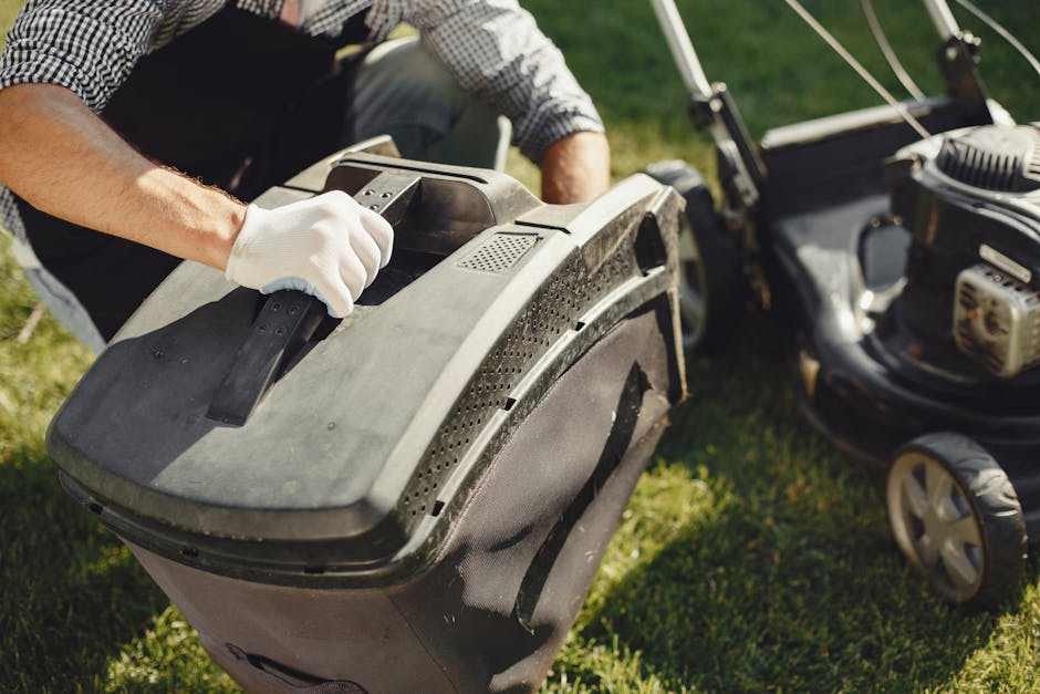 A person wearing white gloves is seen adjusting the handle of a large, black robotic lawn mower situated on a well-maintained garden lawn. In the background, there is a lawnmower with a gasoline engin